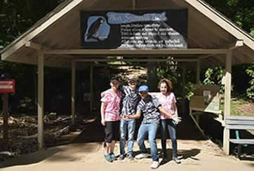 Pinnacle Mountain group in pink or grey tye dyed shirts posing in front of entrance to West Summit Trail
