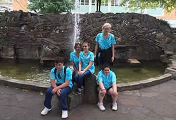 Mount Ida group students and staff in blue tye dyed shirts pose for photo in front of water fountain