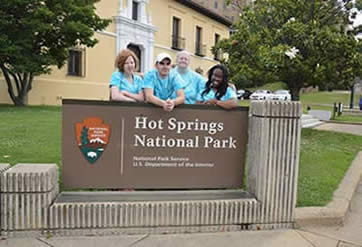 Students and staff in blue tye dyed shirts stand behind Hot Springs National Park sign