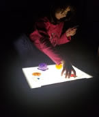 A little girl in a pink shirt uses the APH Light Box Kit in a darkened room